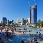 South Bank Beach in Brisbane mit vielen Badegästen, Palmen und der Skyline der Stadt im Hintergrund.