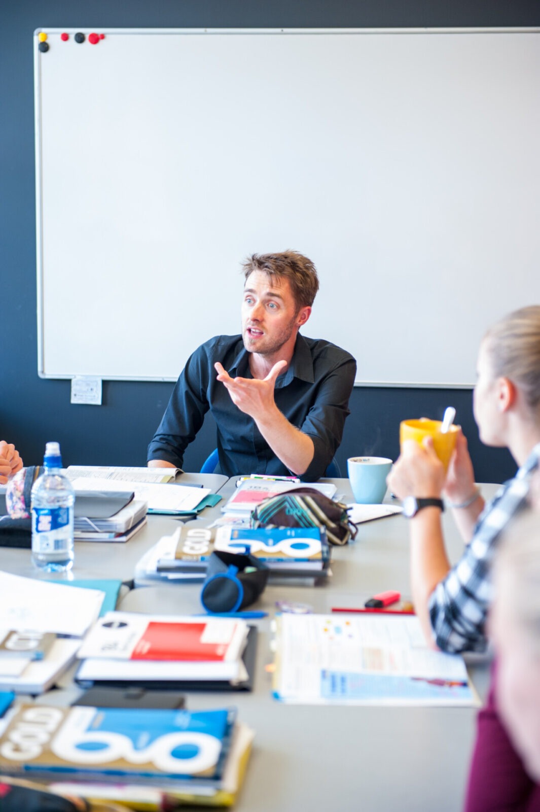 Ein engagierter Dozent oder Teamleiter spricht mit einer Gruppe von Studierenden oder Kollegen in einem modernen Seminarraum mit Whiteboard.