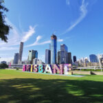 Bunte „Brisbane“-Buchstaben mit Skyline der Stadt im Hintergrund bei blauem Himmel