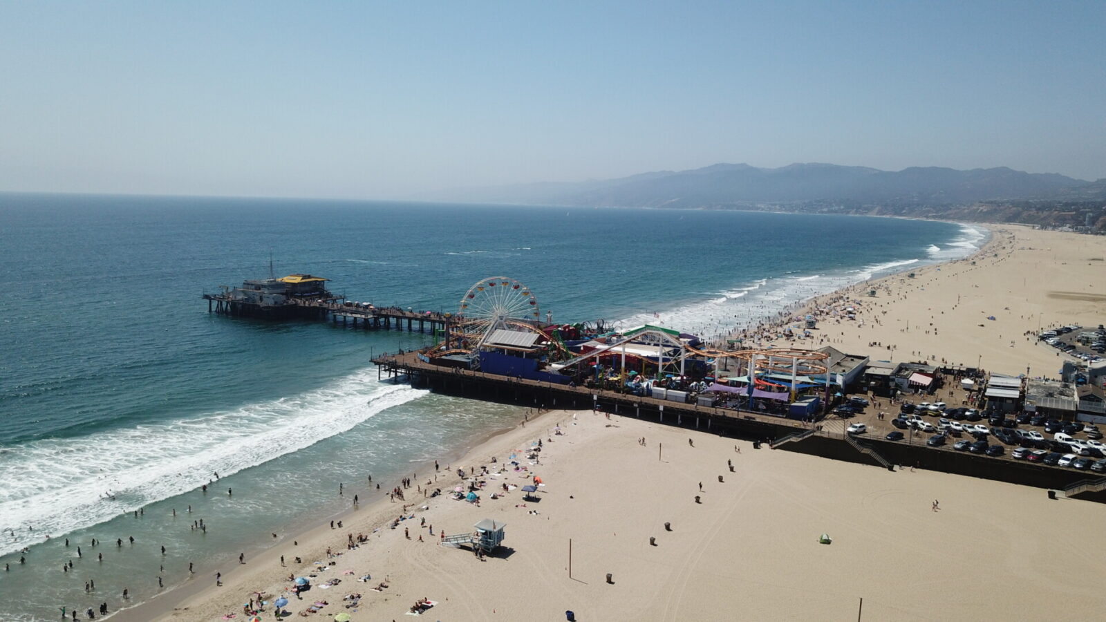 Luftaufnahme des Santa Monica Pier mit Vergnügungspark, Sandstrand und Wellen des Pazifischen Ozeans.