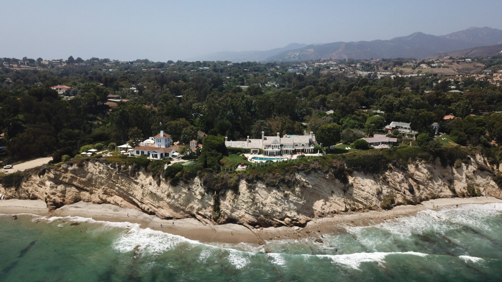 Luxuriöse Villen auf einer Klippe mit Blick auf den Pazifik in Malibu, Kalifornien, umgeben von grünen Hügeln und Strand.