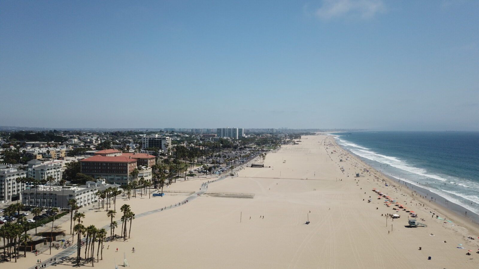 Luftaufnahme des Santa Monica Beach in Los Angeles mit Sandstrand, Pazifik und Palmen unter klarem Himmel.