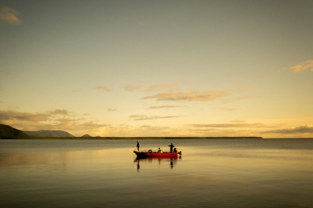 Fischer auf einem kleinen Boot in ruhigem Wasser bei Sonnenuntergang, umgeben von einer malerischen Landschaft.