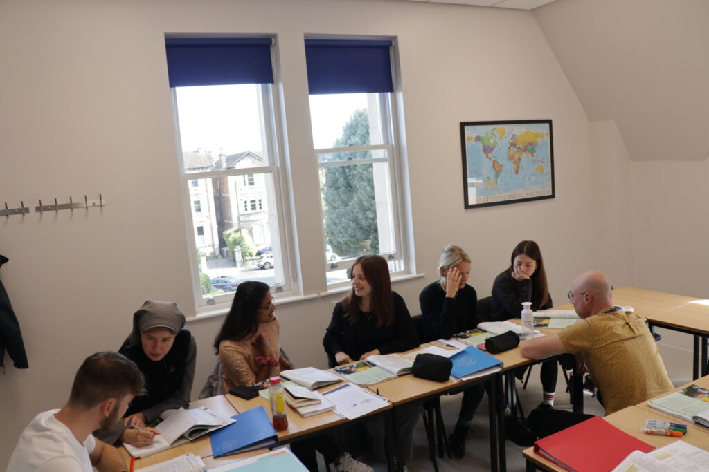 Studierende arbeiten in einer Gruppenübung mit ihrem Lehrer in einem hellen Klassenzimmer.