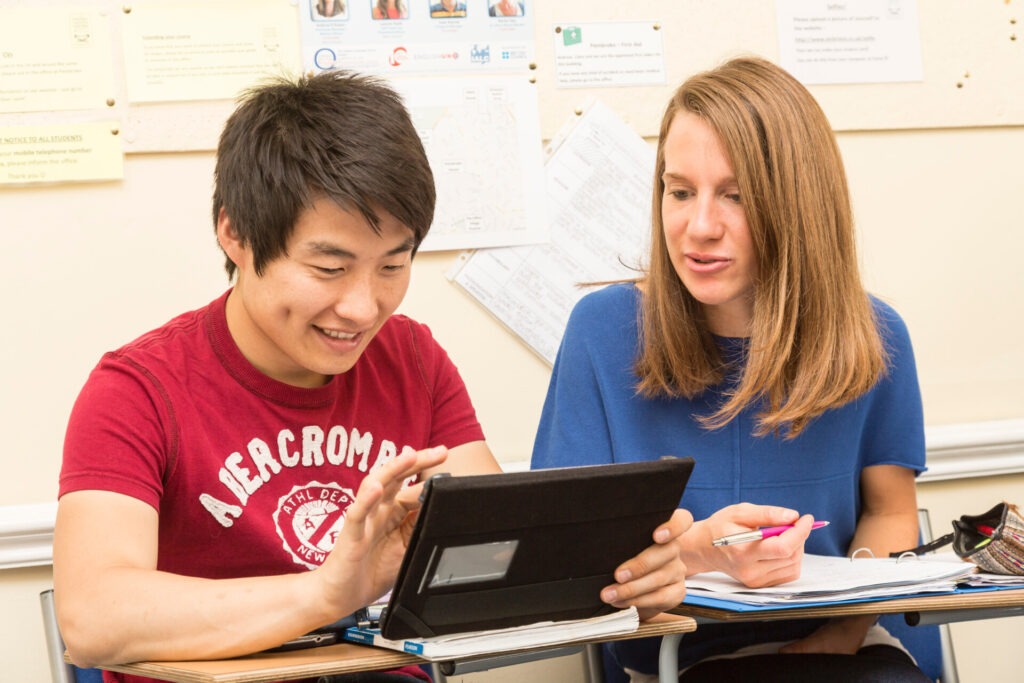 Zwei Studierende arbeiten gemeinsam an einem Tablet in einem Klassenzimmer.