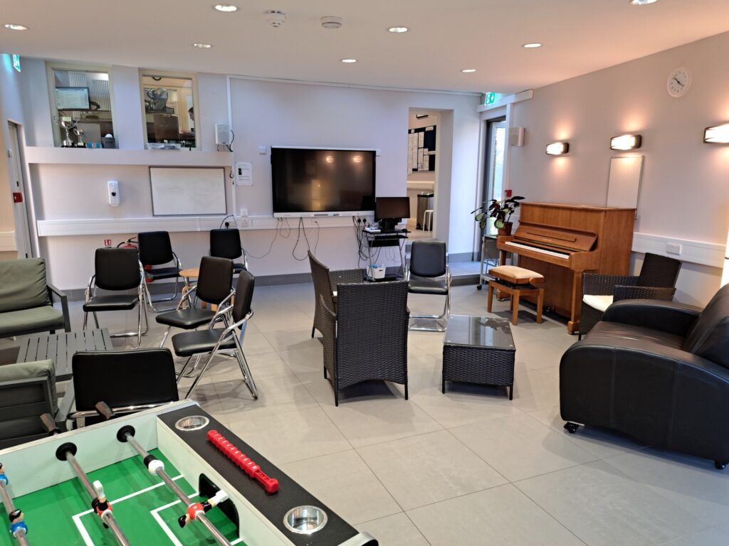 Gemütlicher Aufenthaltsraum mit Sitzgelegenheiten, Klavier, Tischkicker und Fernseher in einer Sprachschule.