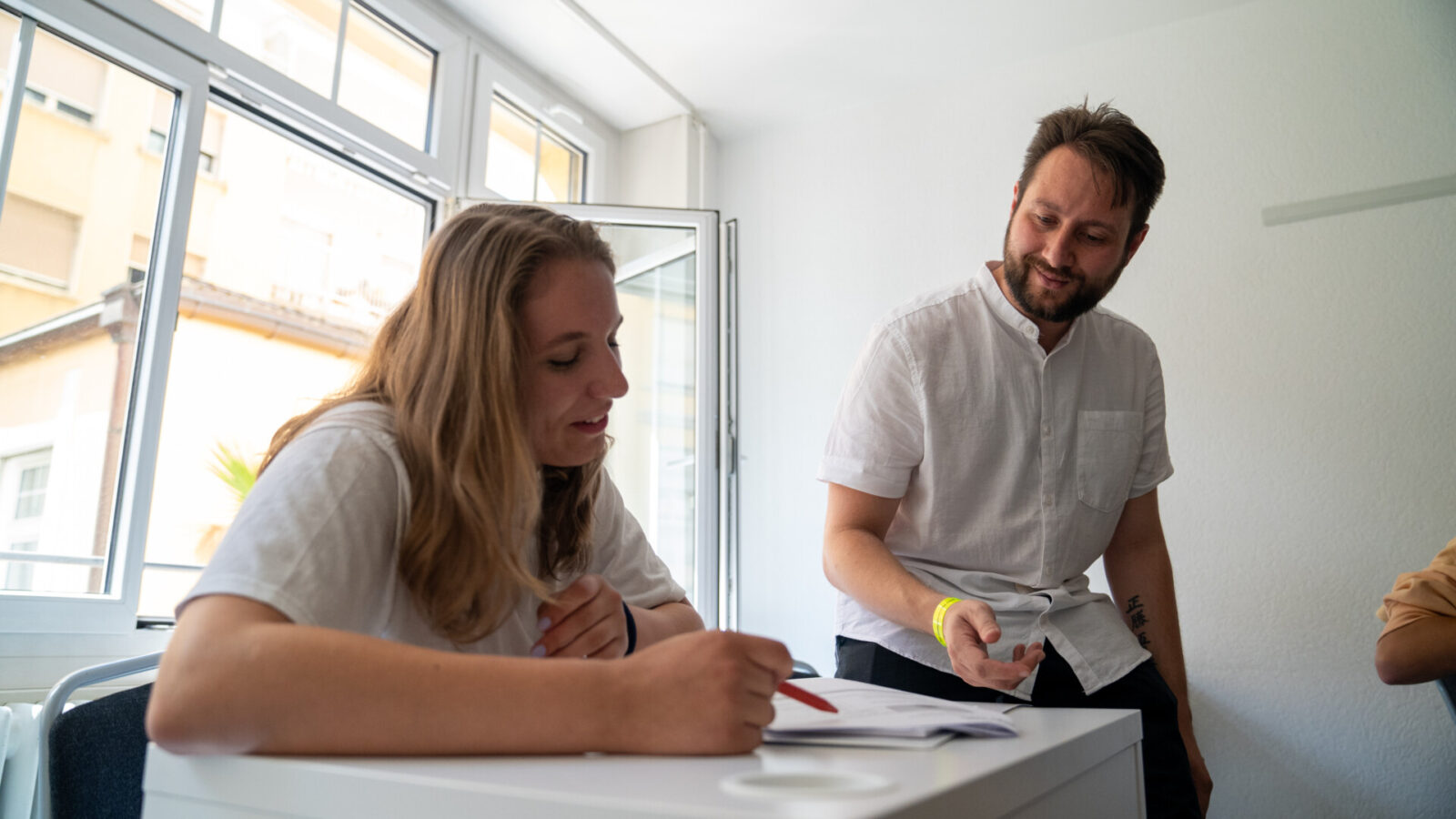 Lehrer hilft einer Schülerin mit Erklärungen während des Unterrichts in einem hellen Klassenzimmer.