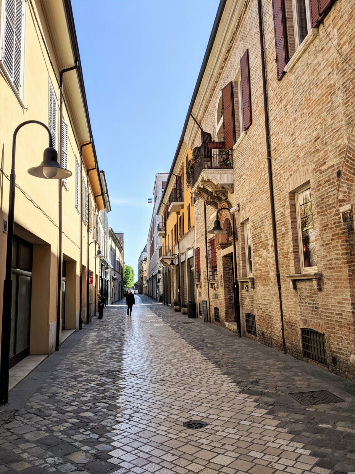 Malerische gepflasterte Gasse mit historischen Gebäuden und Balkonen unter blauem Himmel.