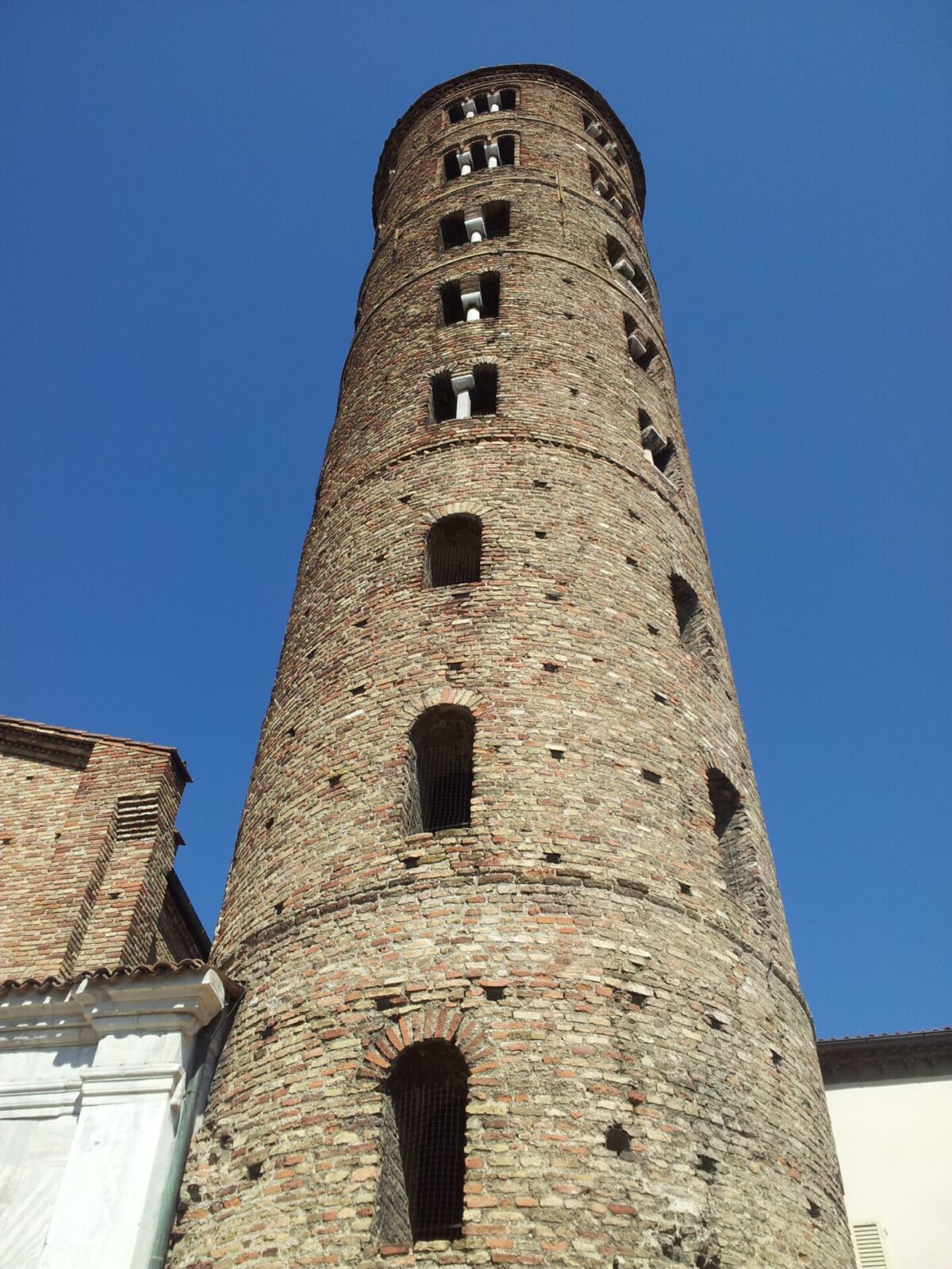 Mittelalterlicher Backsteinturm mit schmalen Fenstern vor blauem Himmel.