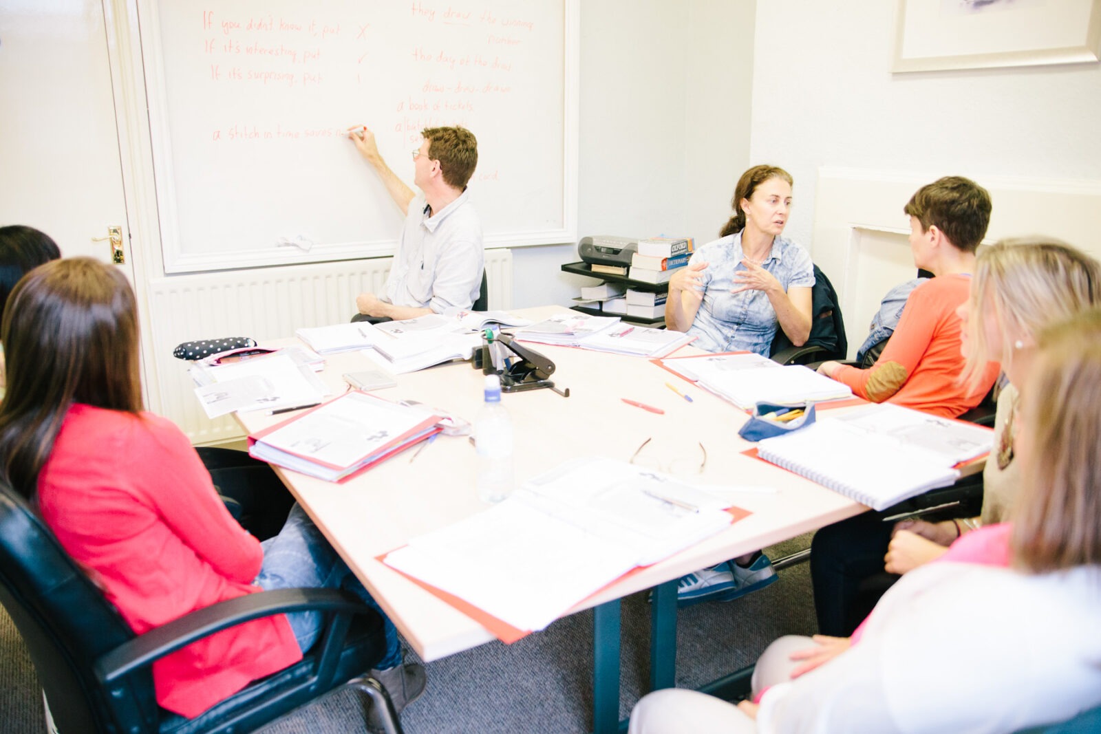 Englischunterricht in einer kleinen Gruppe mit Lehrer, der an der Tafel erklärt.