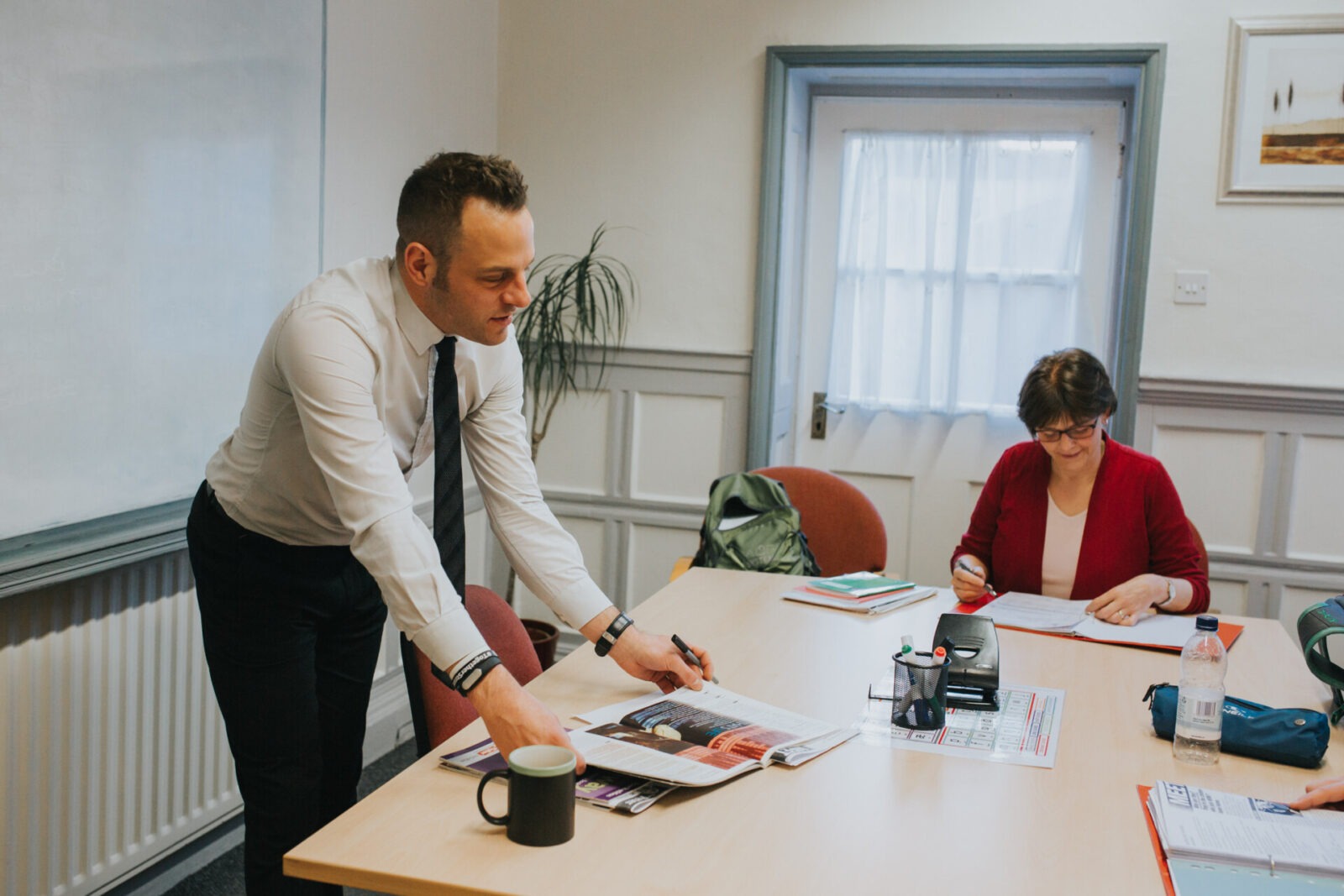 Ein Englischlehrer erklärt einer erwachsenen Schülerin eine Übung in einem Klassenzimmer.
