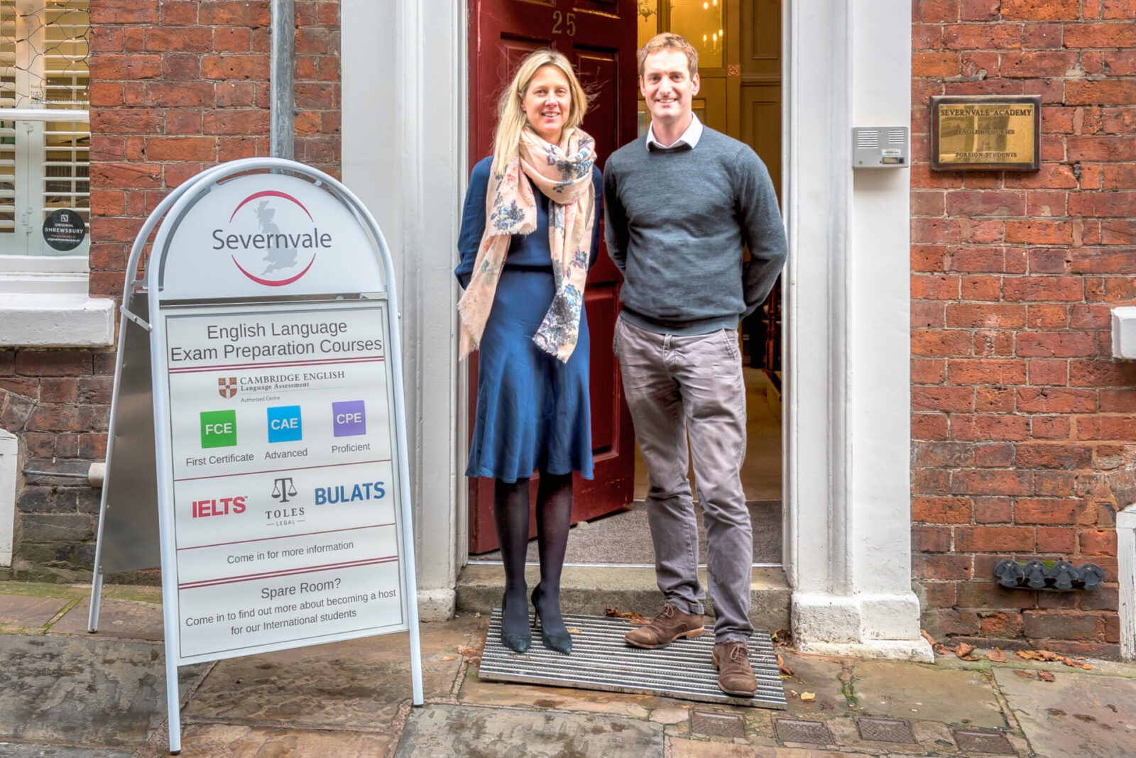 Zwei Mitarbeiter der Severnvale Academy stehen lächelnd vor dem Eingang der Sprachschule in Shrewsbury.