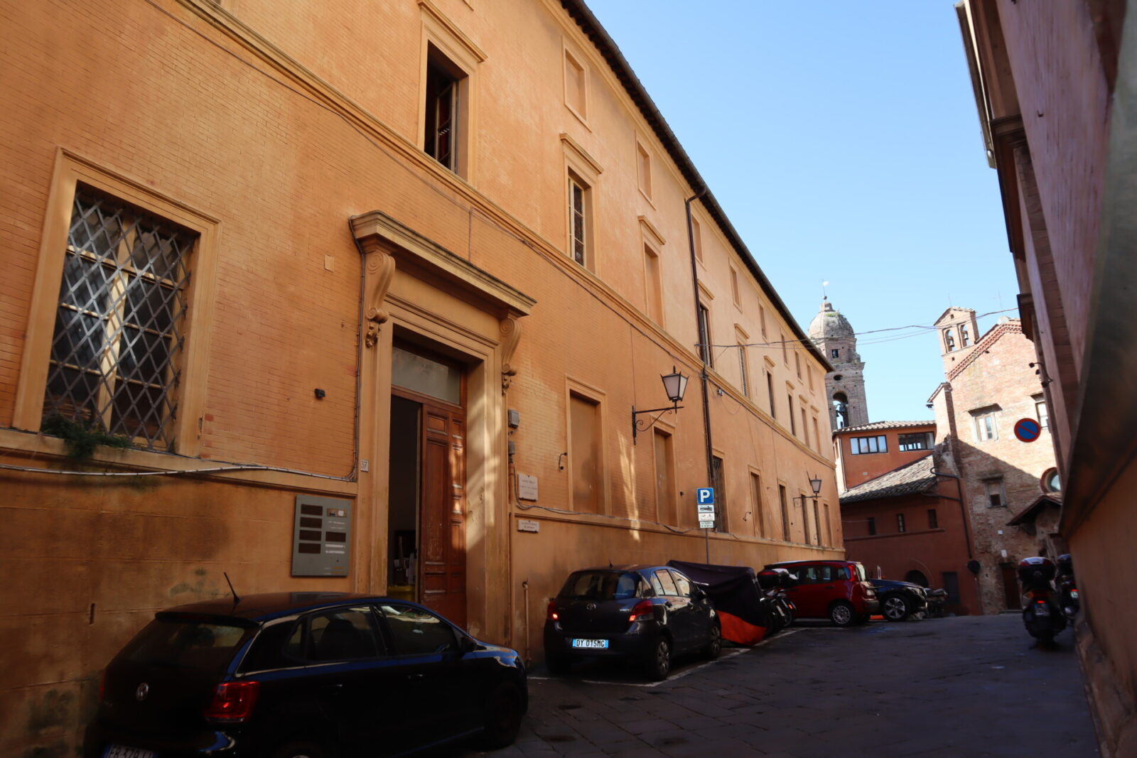 Historisches Gebäude mit orangefarbener Fassade in einer engen Straße mit parkenden Autos in Italien.
