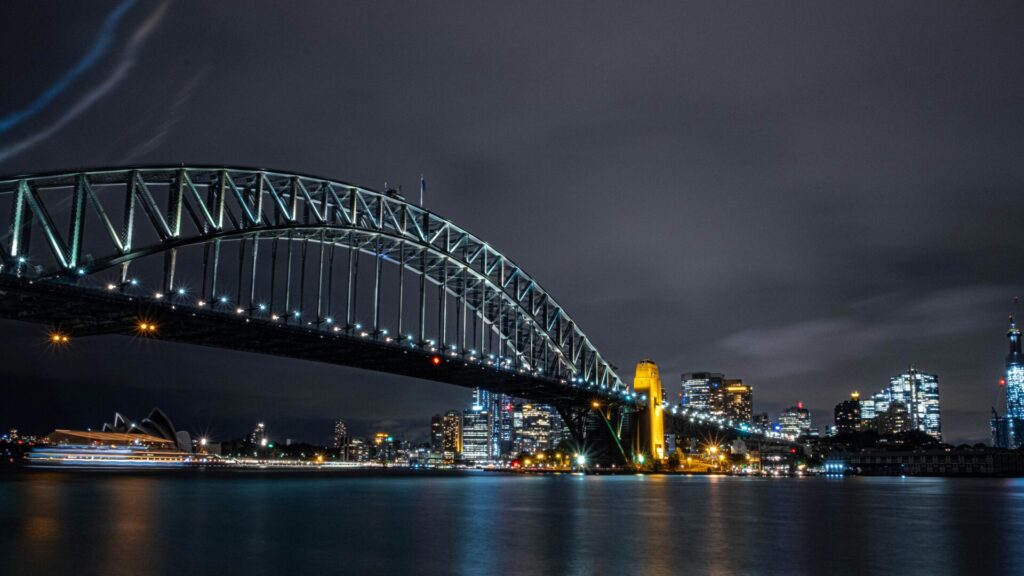 Sydney Harbour Bridge bei Nacht mit beleuchteter Skyline und Opernhaus.