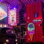 Bunte Neonlichter bei Nacht in der Kombi Alley mit Streetfood-Ständen und VW-Bus