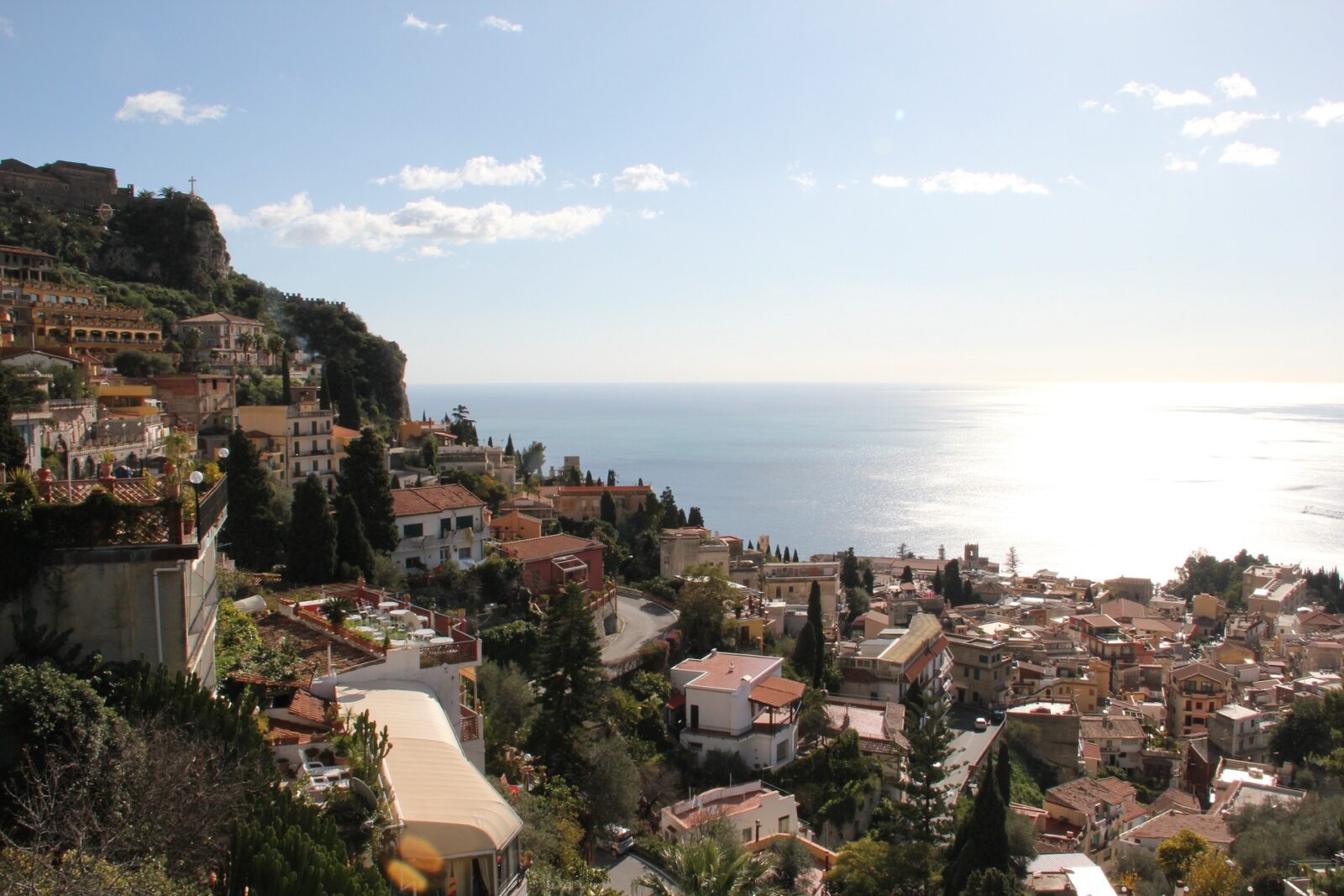 Panoramablick auf Taormina mit malerischen Häusern und dem glitzernden Mittelmeer im Hintergrund.