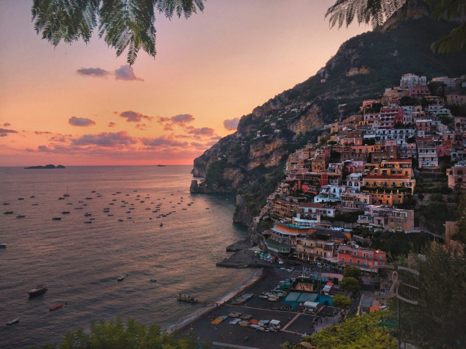 Romantischer Sonnenuntergang über Positano an der Amalfiküste mit bunten Häusern an der Steilküste und Booten im Meer.