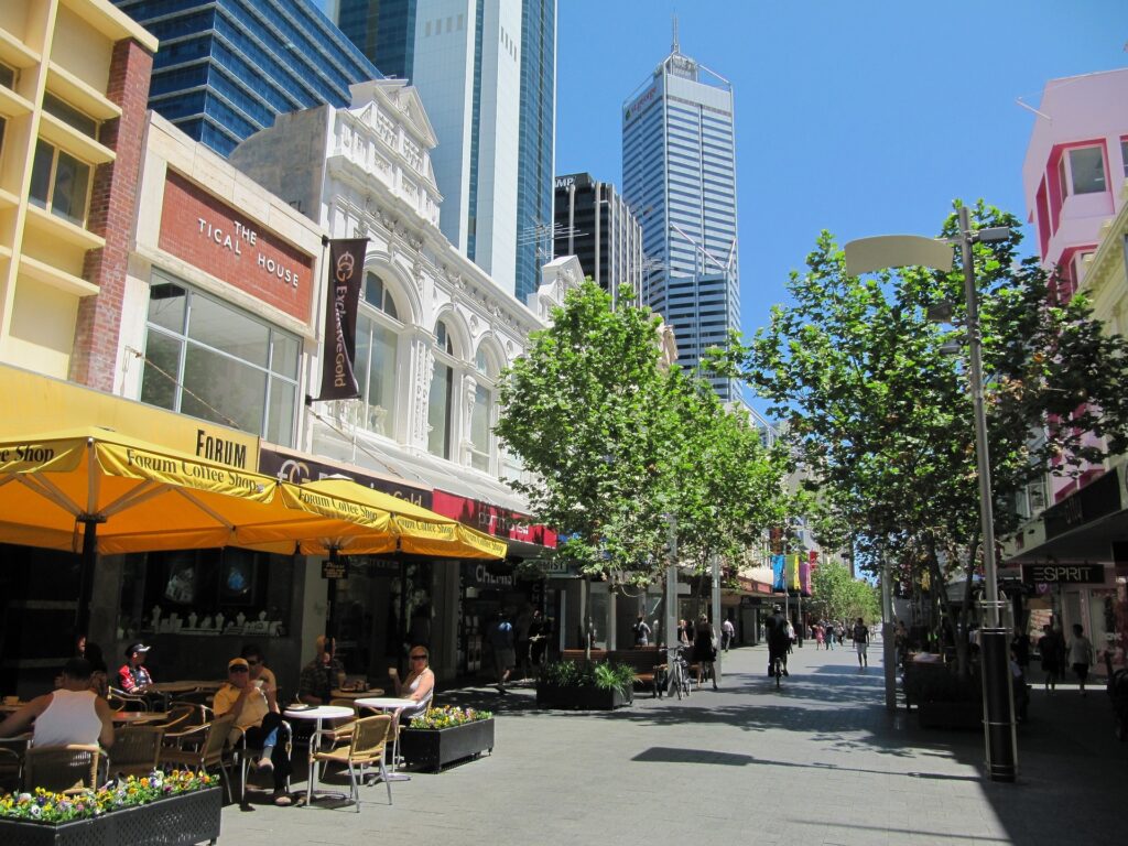 Fußgängerzone in Perth mit Straßencafés, Geschäften und moderner Architektur im Hintergrund.