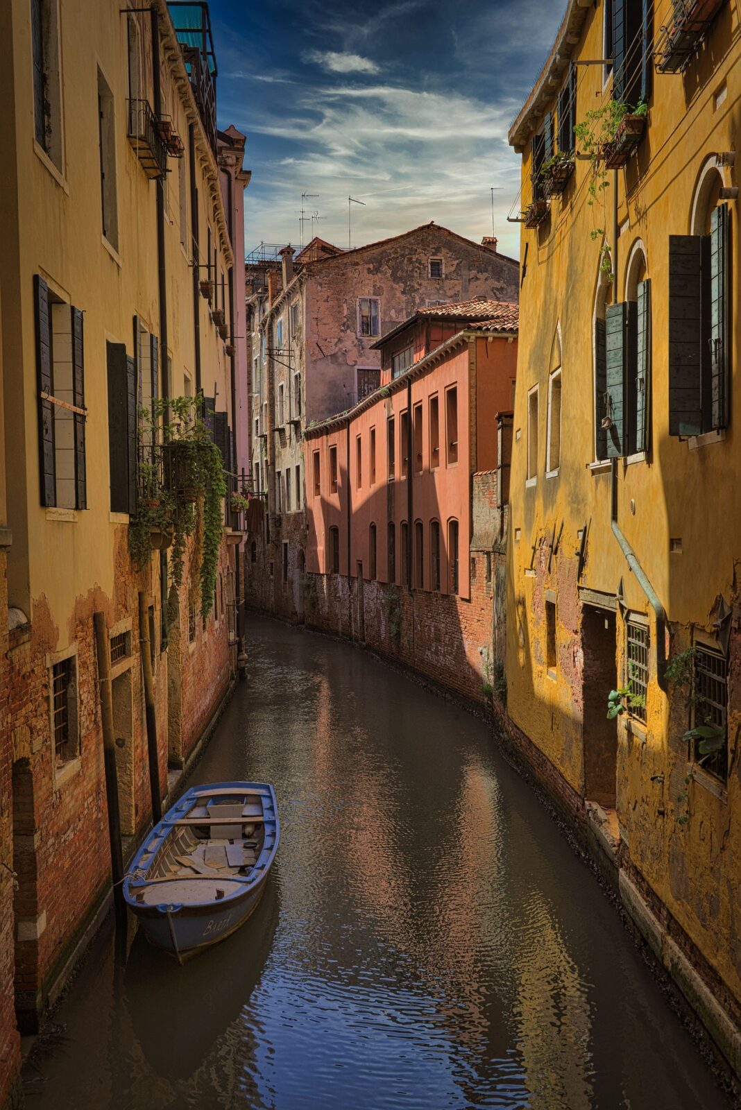 Schmaler venezianischer Kanal mit farbenfrohen, historischen Häusern und einem verlassenen Boot im ruhigen Wasser.