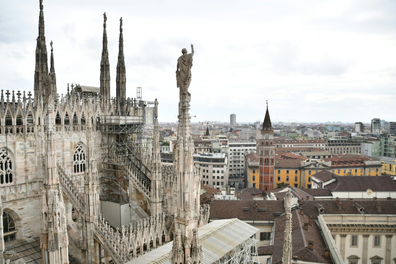 Blick von den Terrassen des Mailänder Doms mit gotischen Statuen und der Skyline von Mailand im Hintergrund.