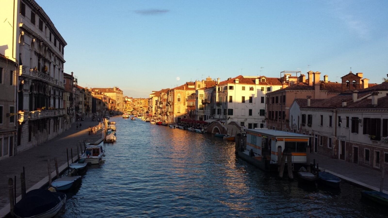 Venezianischer Kanal im warmen Abendlicht mit historischen Gebäuden, Booten und einer Vaporetto-Haltestelle.