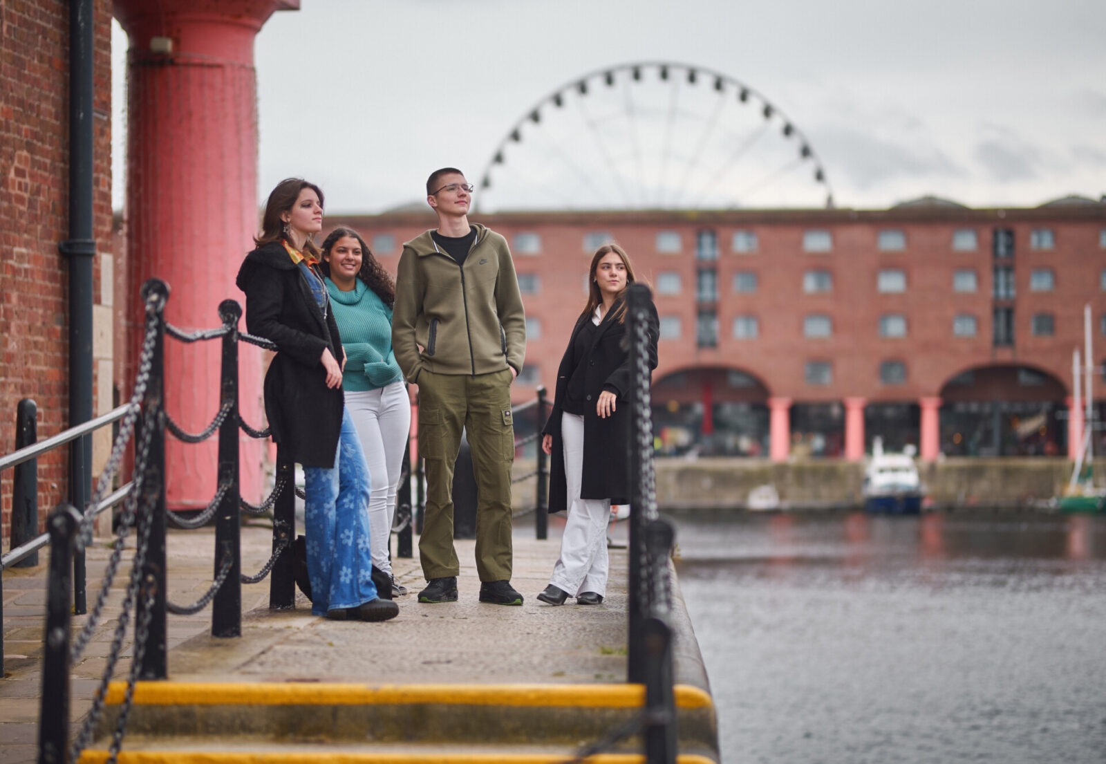 Junge Menschen genießen die Aussicht am Albert Dock in Liverpool mit dem Riesenrad im Hintergrund.