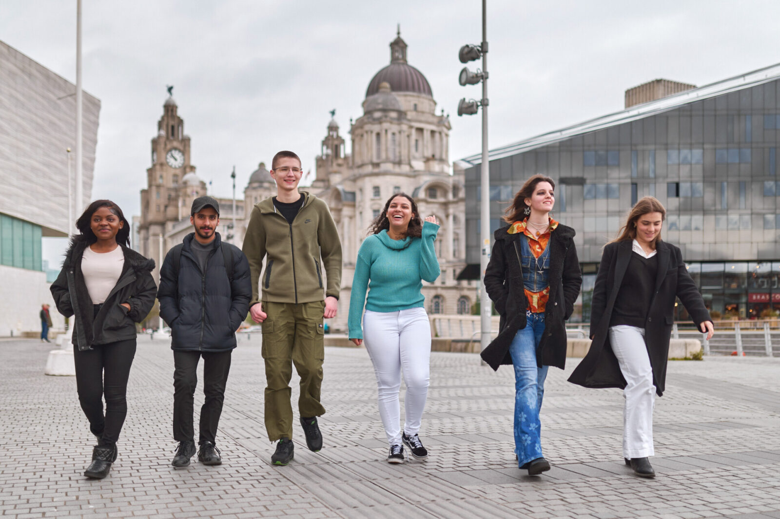 Gruppe junger Menschen spaziert durch Liverpool mit den Three Graces im Hintergrund.