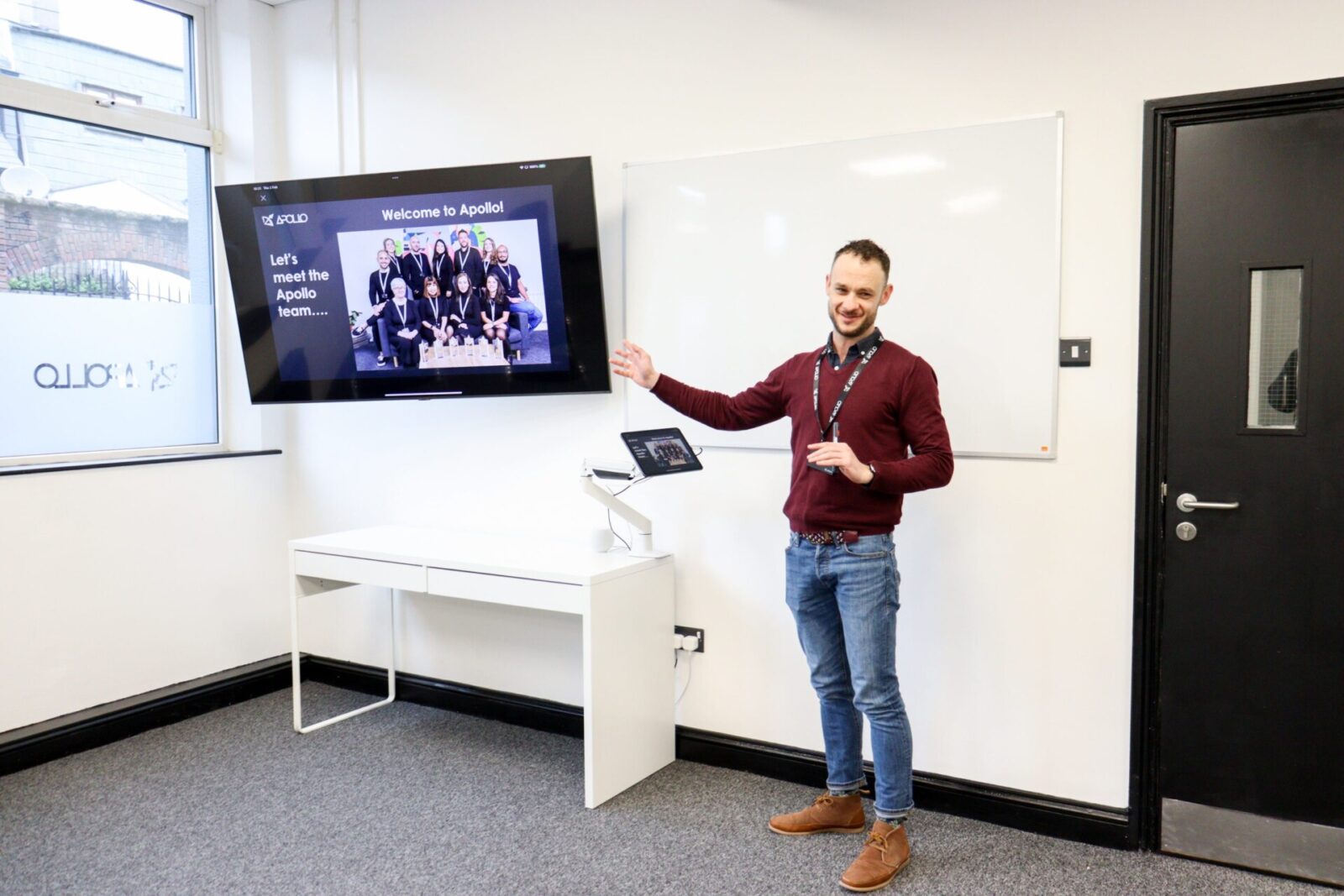 Mitarbeiter von Apollo präsentiert Team-Vorstellung in einem modernen Meetingraum mit Bildschirm und Whiteboard.