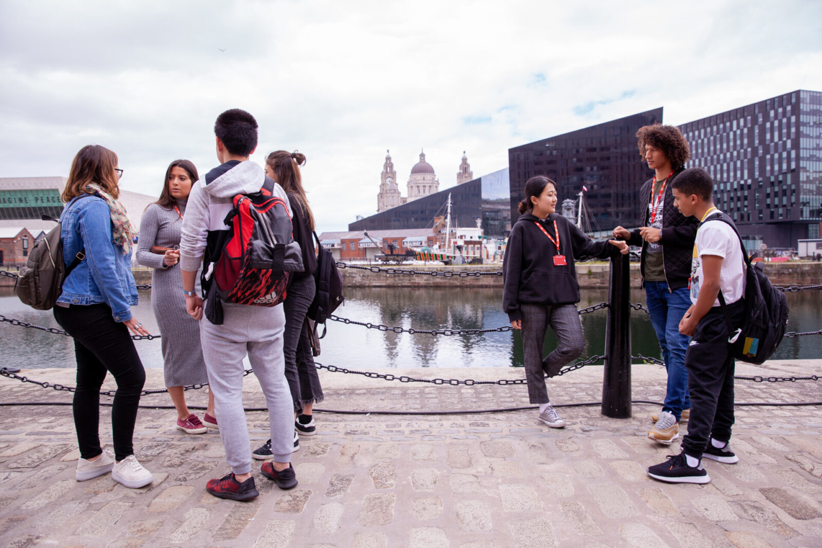 Internationale Studierende genießen eine Stadttour am Liverpool Waterfront mit Blick auf moderne Architektur und historische Wahrzeichen.