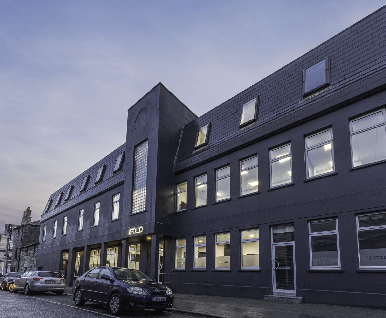 Moderne Firmenzentrale von Apollo mit dunkler Fassade, beleuchteten Fenstern und stilvoller Architektur bei Dämmerung.