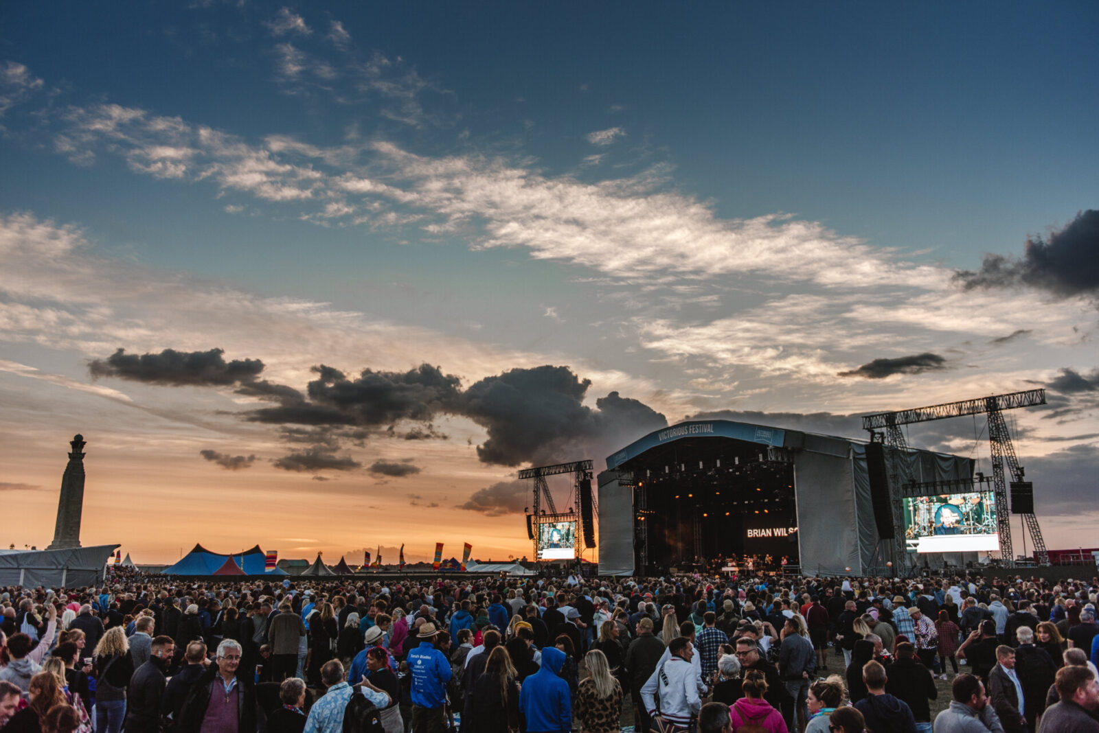 Große Menschenmenge beim Victorious Festival in Portsmouth mit Hauptbühne und Sonnenuntergang im Hintergrund.