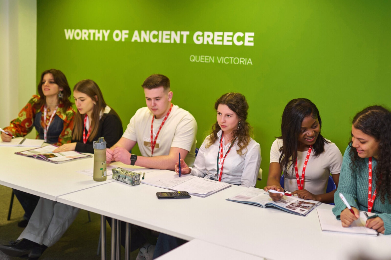 Gruppe von internationalen Studierenden im Klassenzimmer mit grünem Hintergrund und dem Zitat von Queen Victoria.