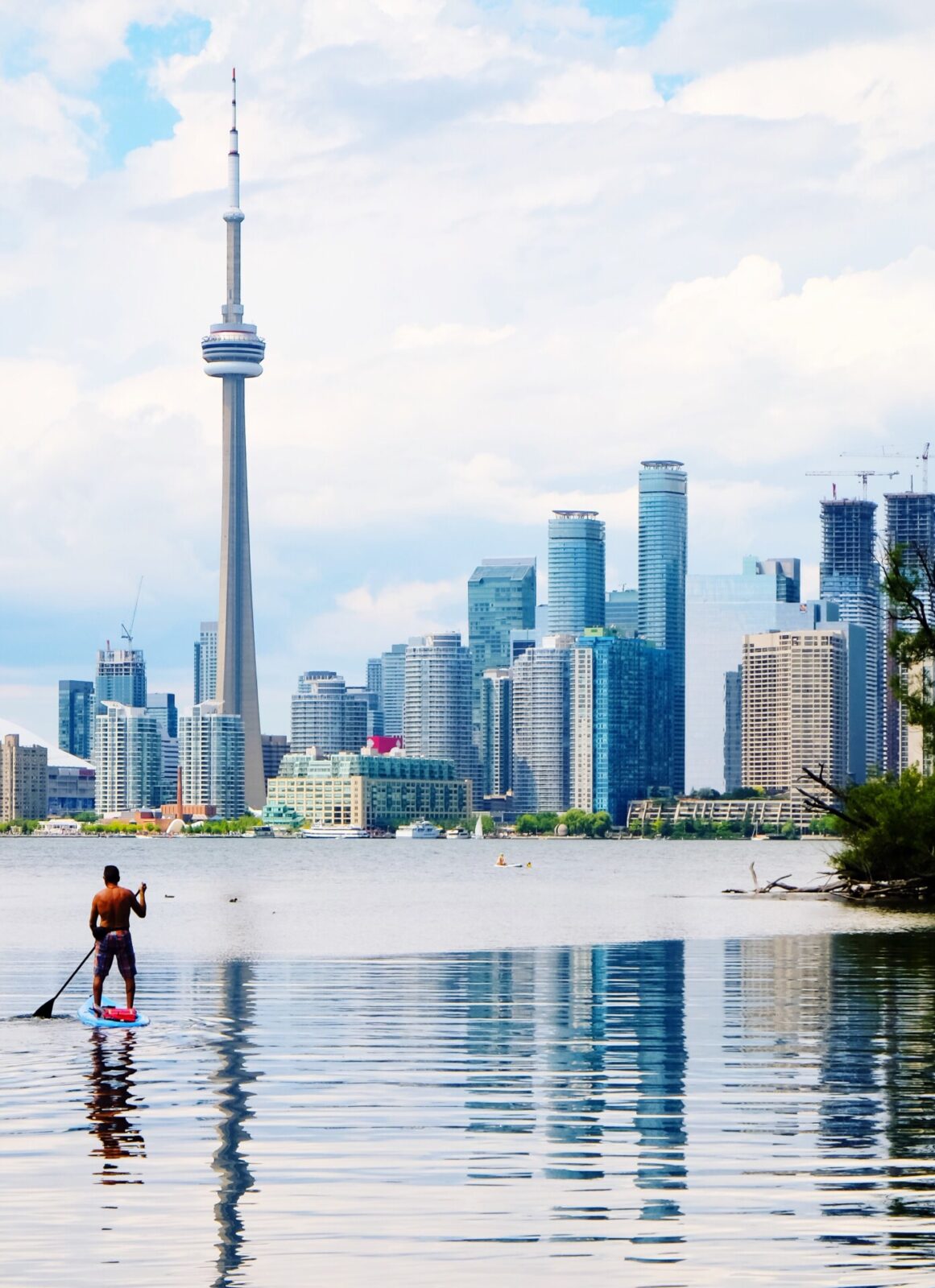 Mann auf einem Stand-Up-Paddle-Board auf dem Wasser mit der Skyline von Toronto und dem CN Tower im Hintergrund.