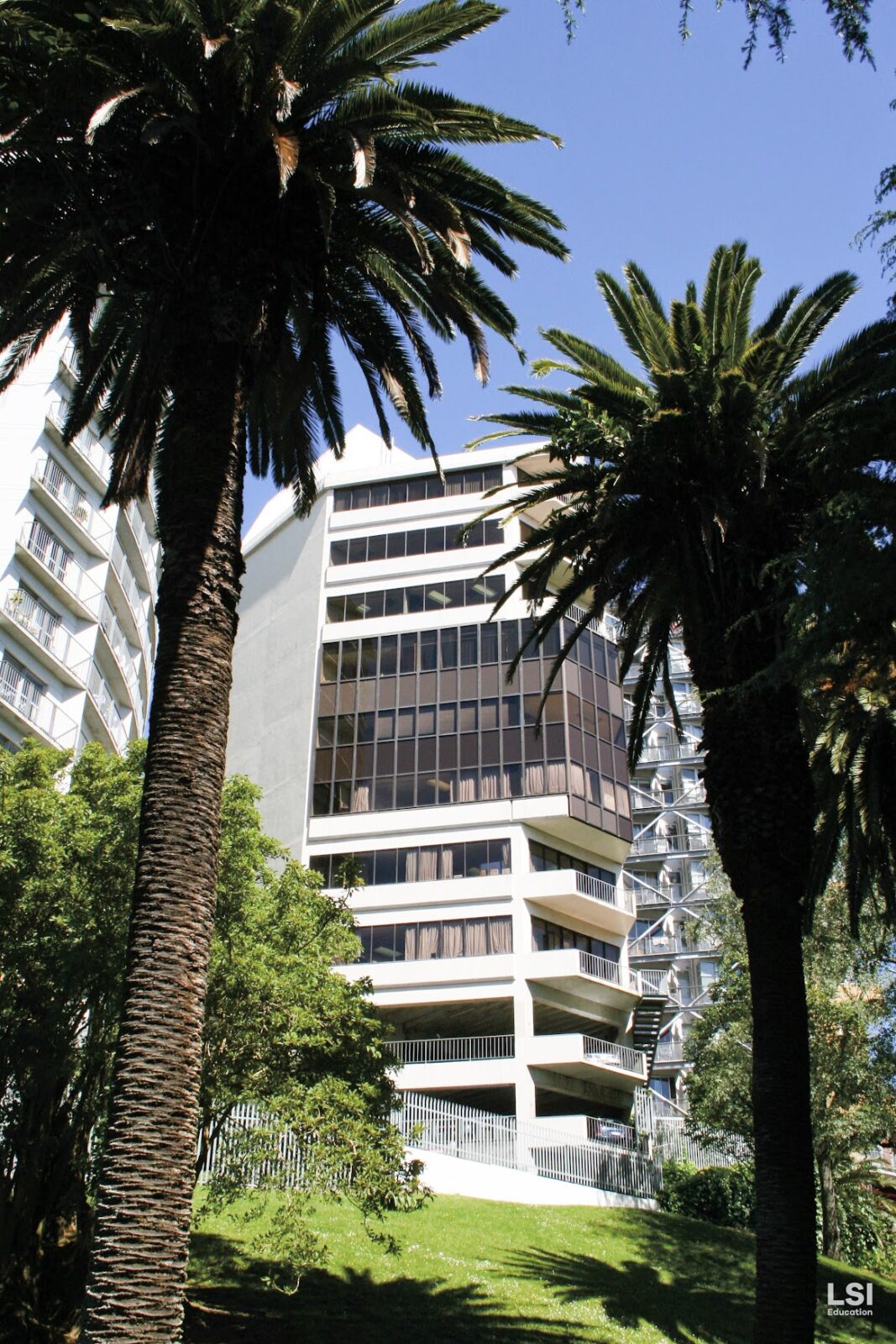 Modernes Gebäude der LSI-Sprachschule, umgeben von Palmen und grüner Natur.